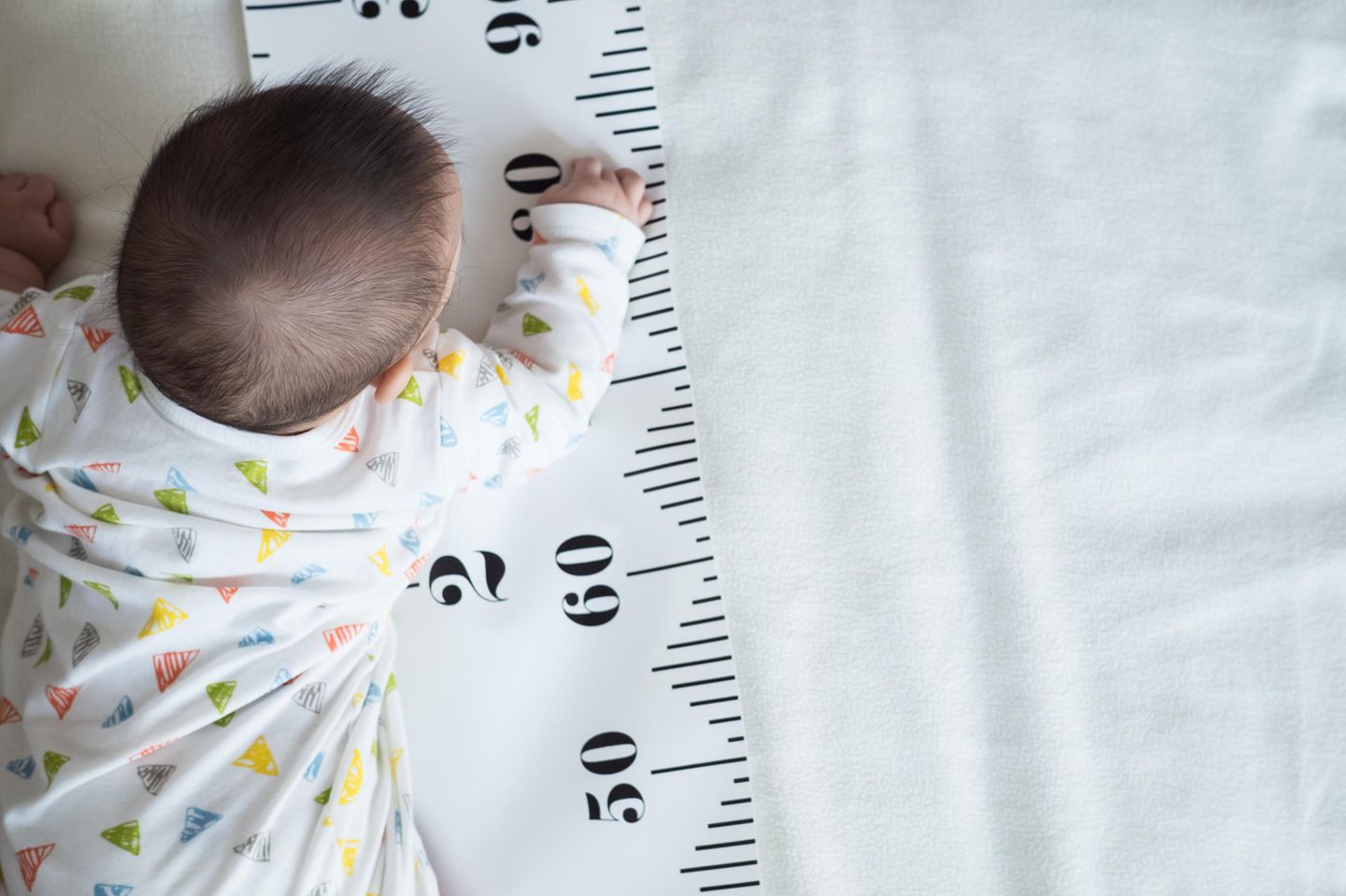 Körpergröße bei Kindern: ein Baby liegt auf einem übergroßen Maßband
