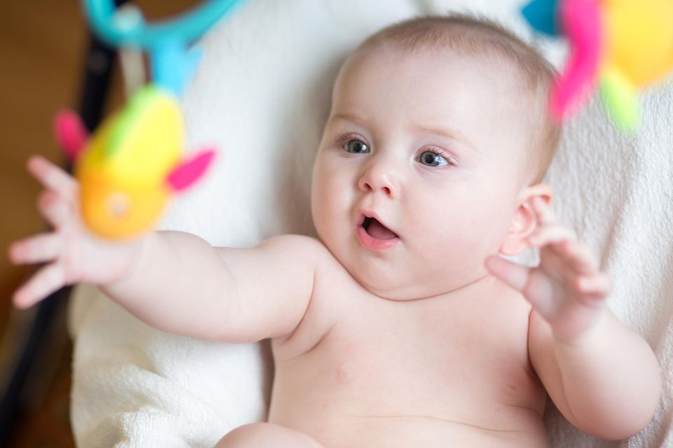 Baby greift  staunend nach buntem Spielzeug