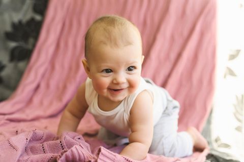 Ein Baby stützt sich mit den Armen ab und lächelt in die Kamera
