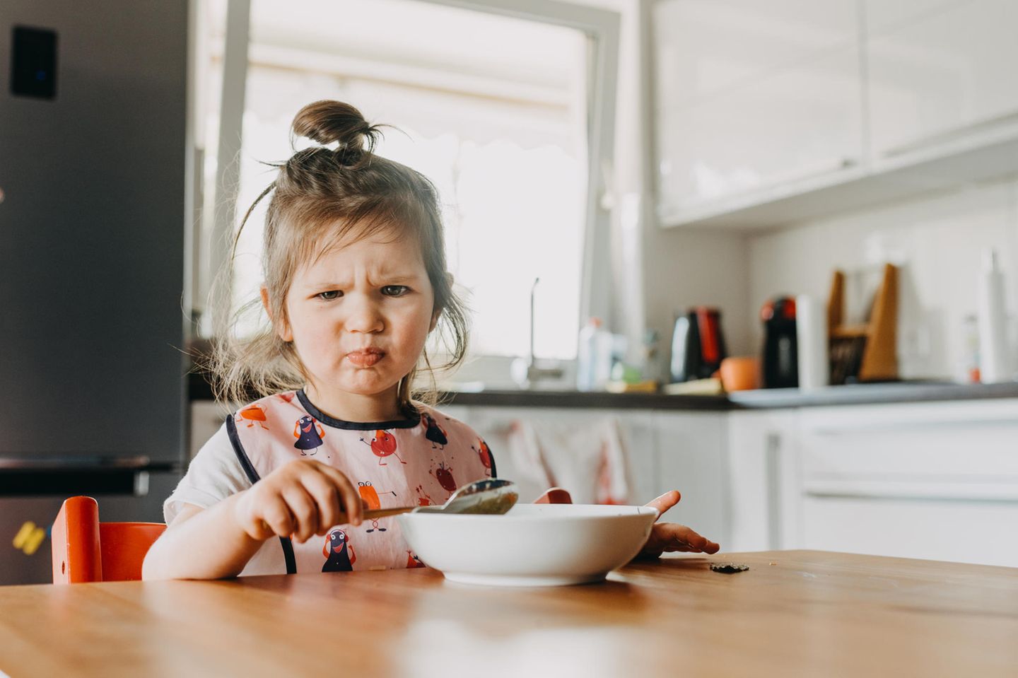 Streitverhalten: ein kleines Mädchen sitzt mit ihrem Essen am Küchentisch und verzieht das Gesicht