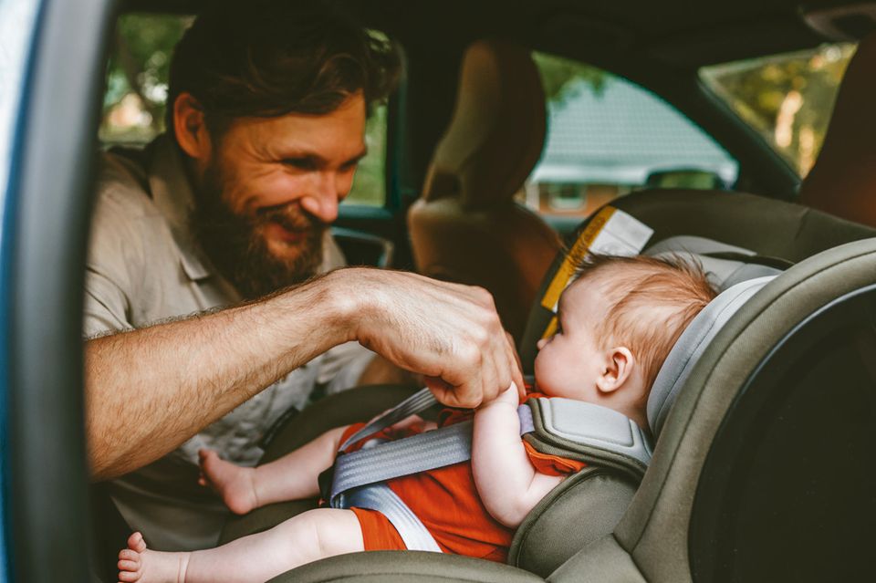 Reboarder-Test: Fröhlicher Vater hält die Hand seines Babys im Reboarder.