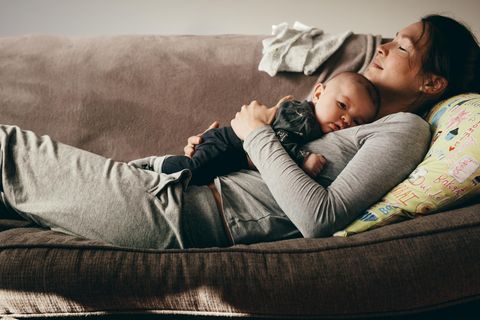 Eltern-Schlaf: eine junge Mutter liegt auf dem Sofa und ihr Baby liegt schlafend auf ihrer Brust