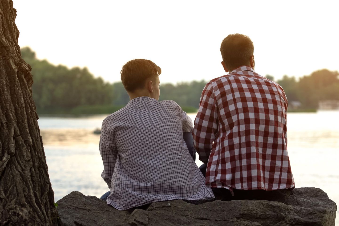 Nicol Ljubic: Vater und sein jugendlicher Sohn sitzen auf einem Baumstamm an einem See