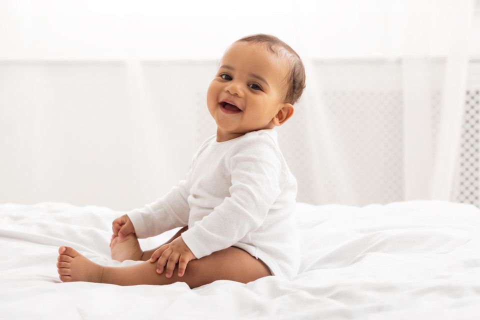 Baby sitzt auf einer weißen Decke und lacht