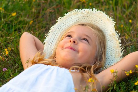 Tagträume: ein kleines Mädchen mit Sonnenhut liegt auf dem Rücken auf einer Wiese