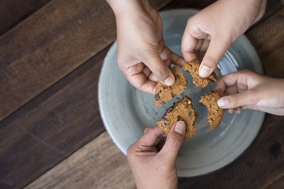 Sharing Economy: vier Hände halten vier Stücke eines Keks über einem Teller