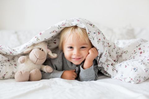 Kinder richtig aufwecken: Kind unter der Decke mit Kuscheltier