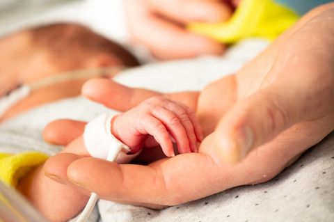 Erwachsenenhand hält Hand des Neugeborenen in der Klinik