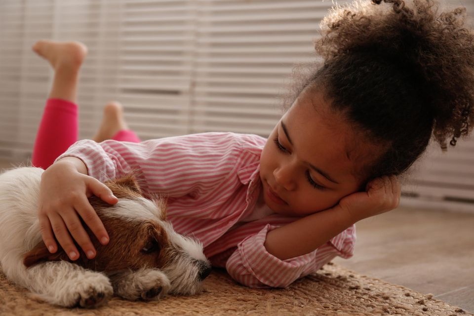 Kleines Mädchen liegt mit einem Hund auf dem Boden und streichelt seinen Kopf