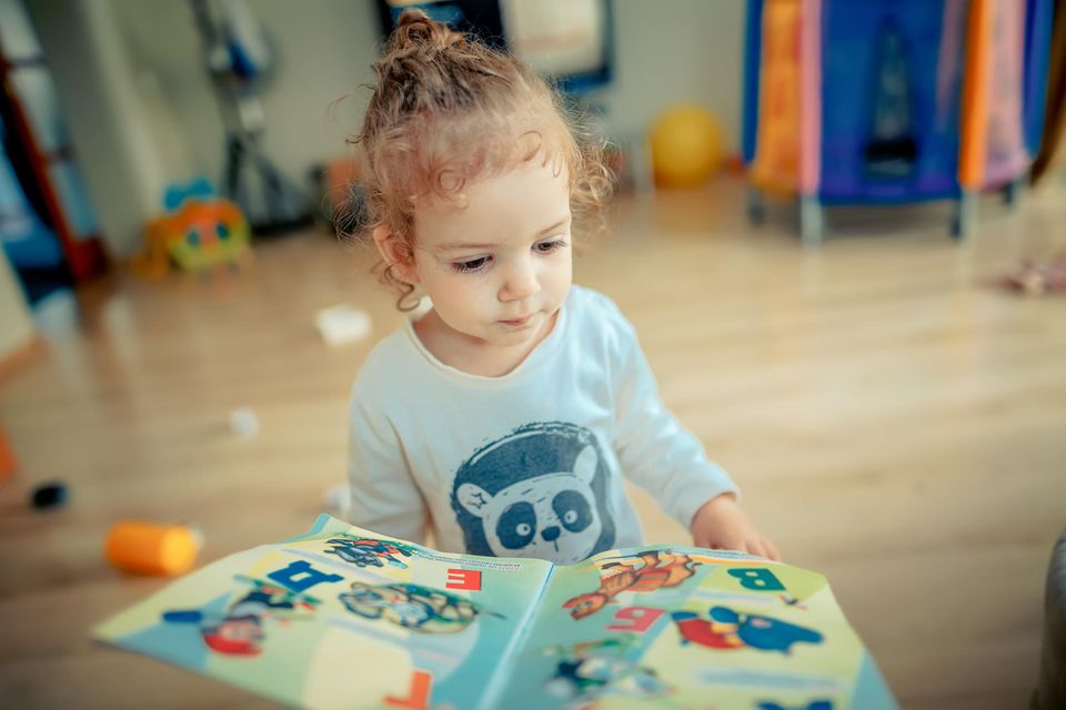 Ukrainische Kinderbücher: Kleines Mädchen schaut sich ABC-Buch mit kyrillischen Buchstaben an.