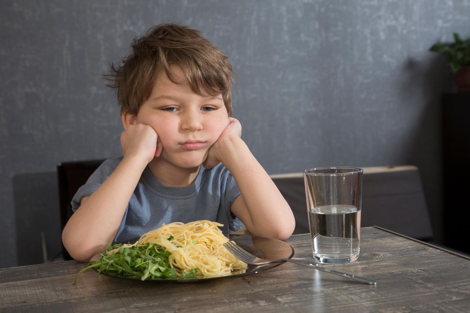 Junge sitzt vor einem Teller Spaghetti und macht ein unglückliches Gesicht.