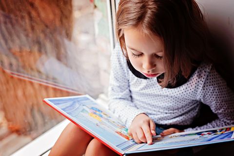 Welttag des Buches: Mädchen am Fenster liest ein Bilderbuch.