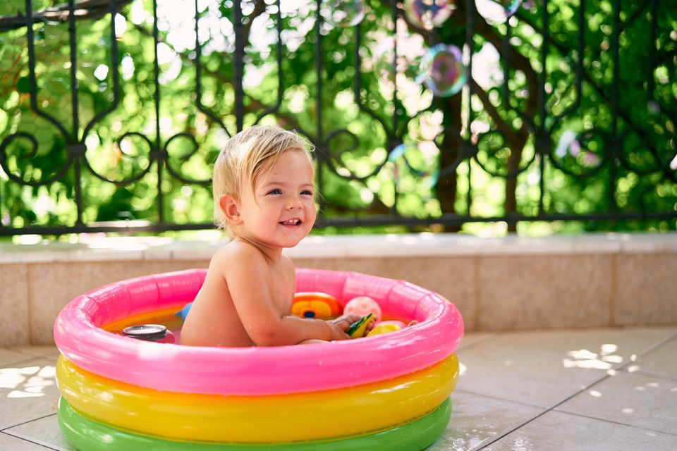 Planschbecken für Kinder: Kind auf Wiese hält Hände in mit Wasser gefülltes Planschbecken.
