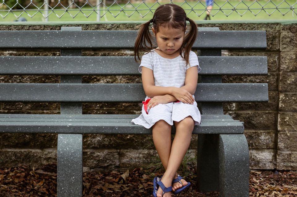 Emotionen managen: Kleines Mädchen sitz verärgert auf einer Bank im Park