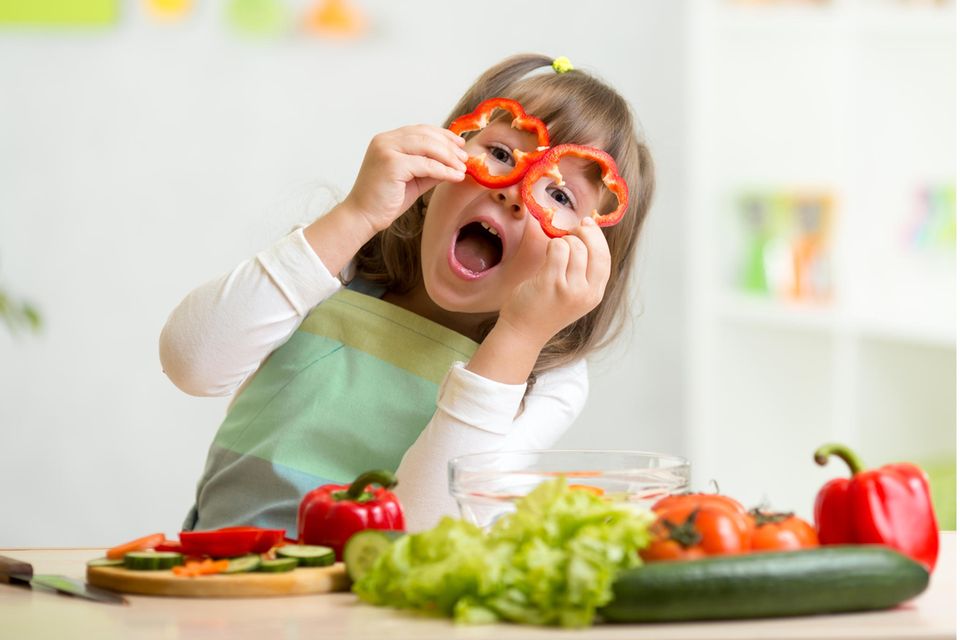 Fleischlos ernähren: Mädchen spielt beim Essen zubereiten mit frischer Paprika