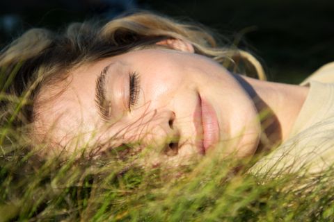 Sonnenschutz fürs Gesicht: Frau liegt in der Sonne im Gras