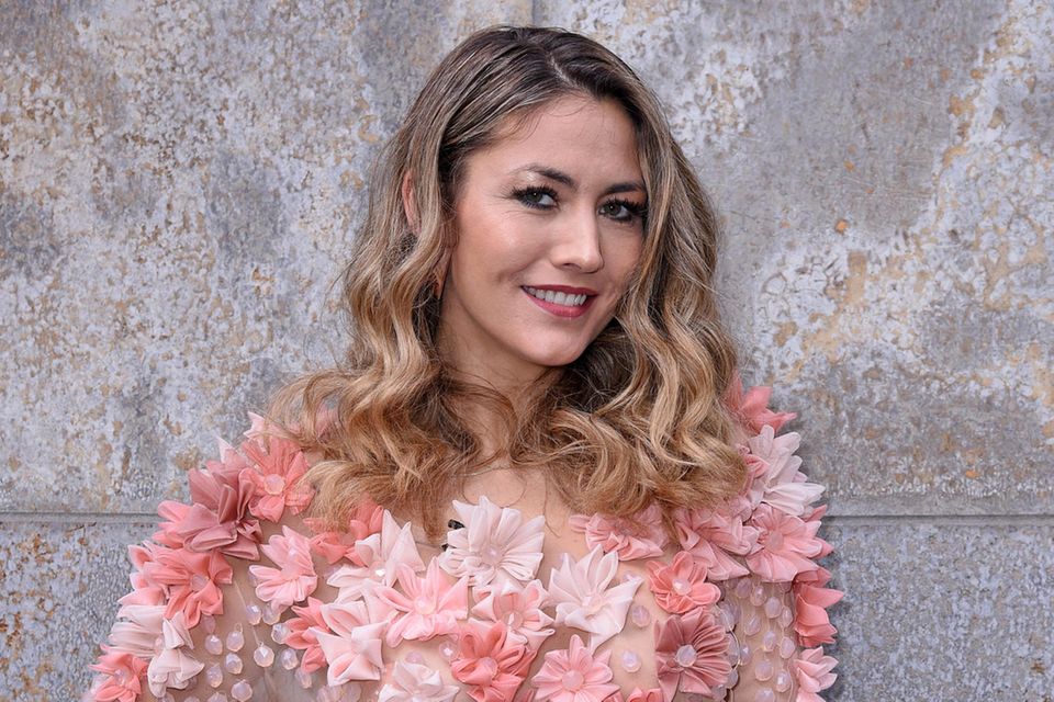 Fiona Erdmann: Fiona Erdmann steht vor einer grauen Wand und trägt ein pinkes Top mit Kunstblumen