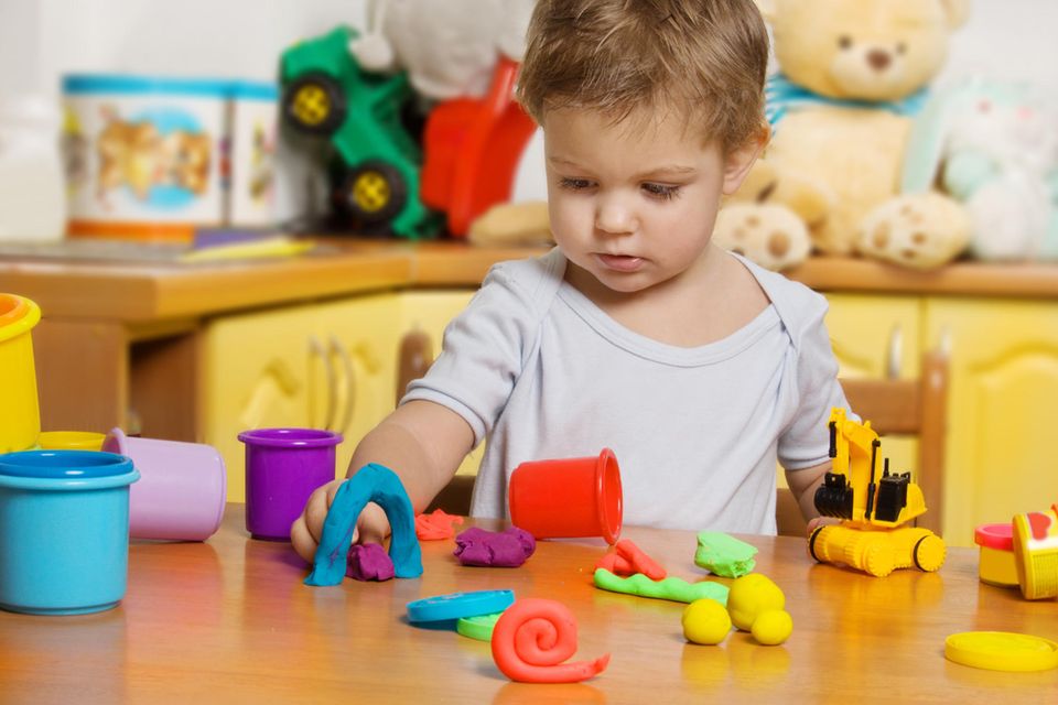 Kinderknete: Kind spielt mit bunter Knete an einem Holztisch.