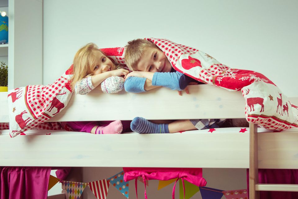 Zwei Kinder sitzen unter einer Decke auf einem Bett