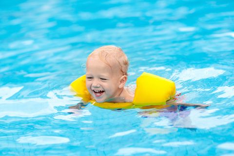 Schwimmflügel-Test: Fröhliches Kind mit gelben Schwimmflügeln im Pool