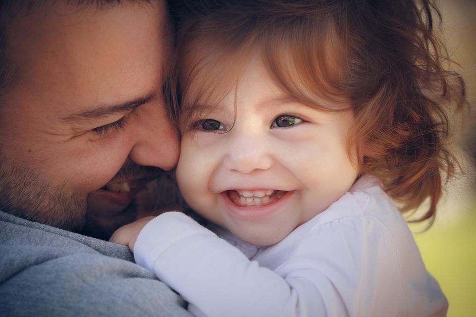 Vater-Kind-Beziehung: Vater hält kleines Kind auf dem Arm und beide lächeln