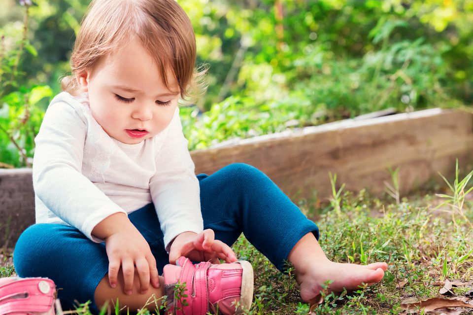 Kleines Mädchen sitzt im Gras und probiert einenn Schuh an