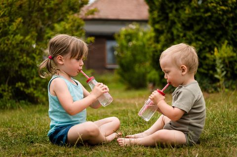 Heiße Sommertage: Zwei kleine Kinder sitzen im Garten und trinken Wasser