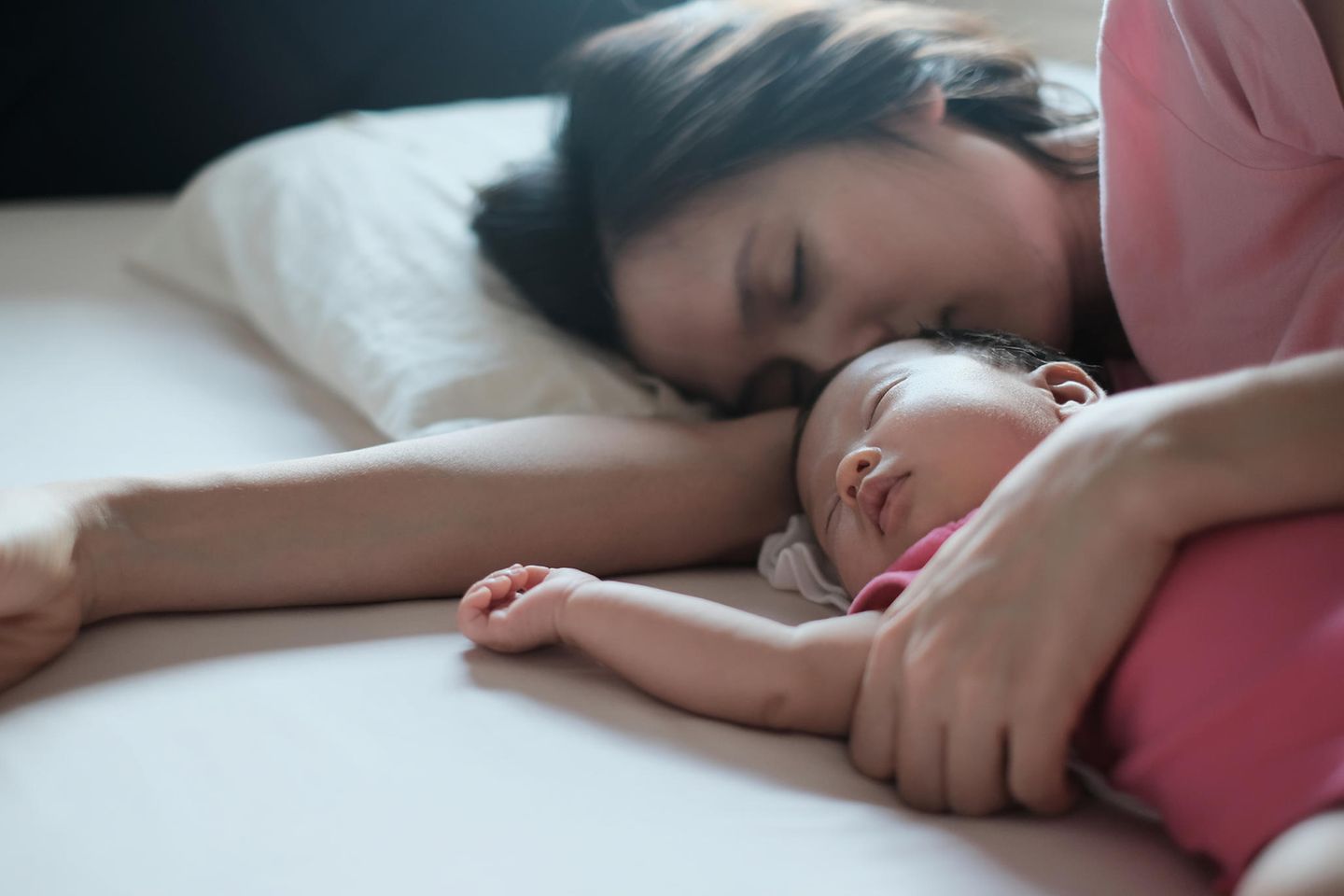 Junge Mama schläft mit ihrem Baby im Arm auf dem Bett