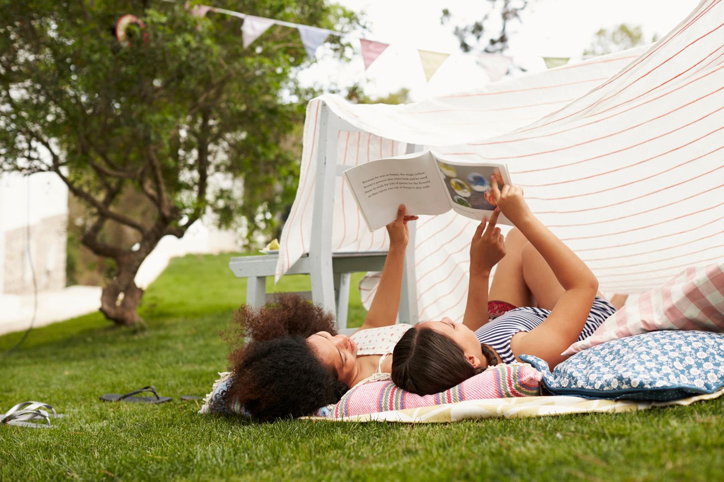 Mutter und Tochter schauen sich auf Picknickdecke ein Kinderbuch im Urlaub an.