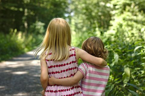 Geschwisterkinder: zwei Geschwister gehen Arm in Arm einen Waldweg hinunter