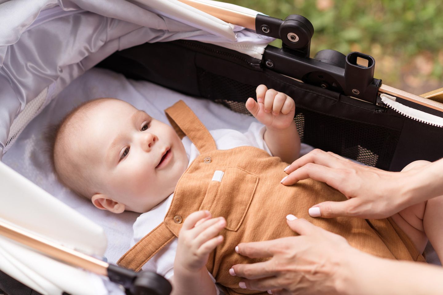 Wickeln unterwegs: Frau spielt mit im Kinderwagen liegenden Baby