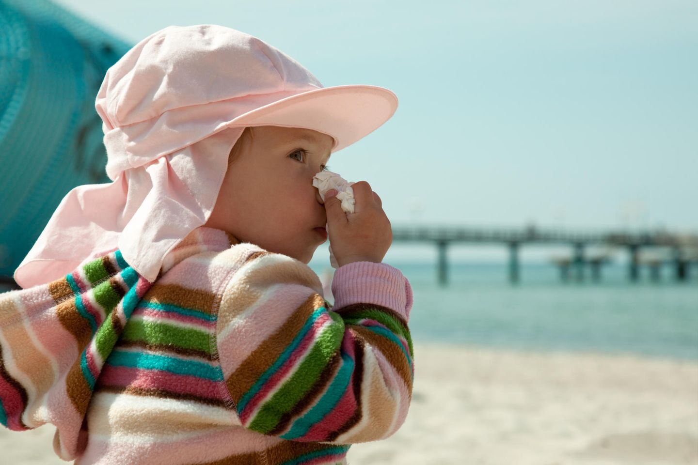Mit einer Reiseapotheke auf Babys Schnupfen vorbereitet: Baby putzt sich die Nase am Strand.