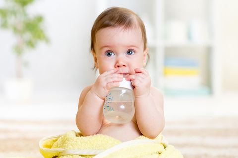 Sitzendes Baby hält wassergefüllte Nuckelflasche