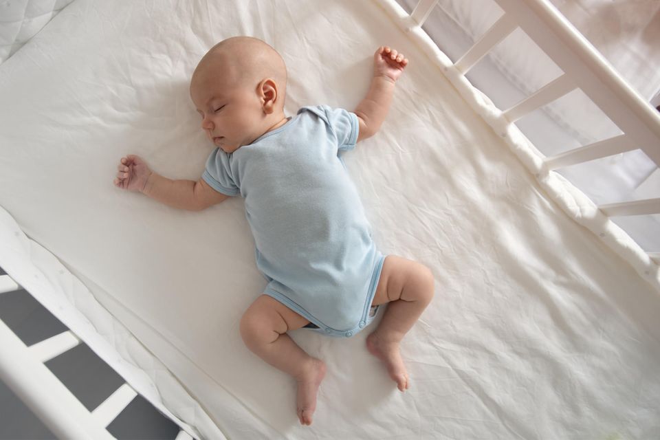 Baby schläft im Body in seinem Babybett