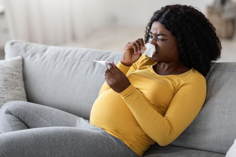 Schwarze schwangere Frau mit Taschentuch und Fieberthermometer