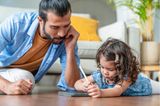 Die Rolle des Vaters: Vater und Tochter machen Homeschooling auf dem Boden