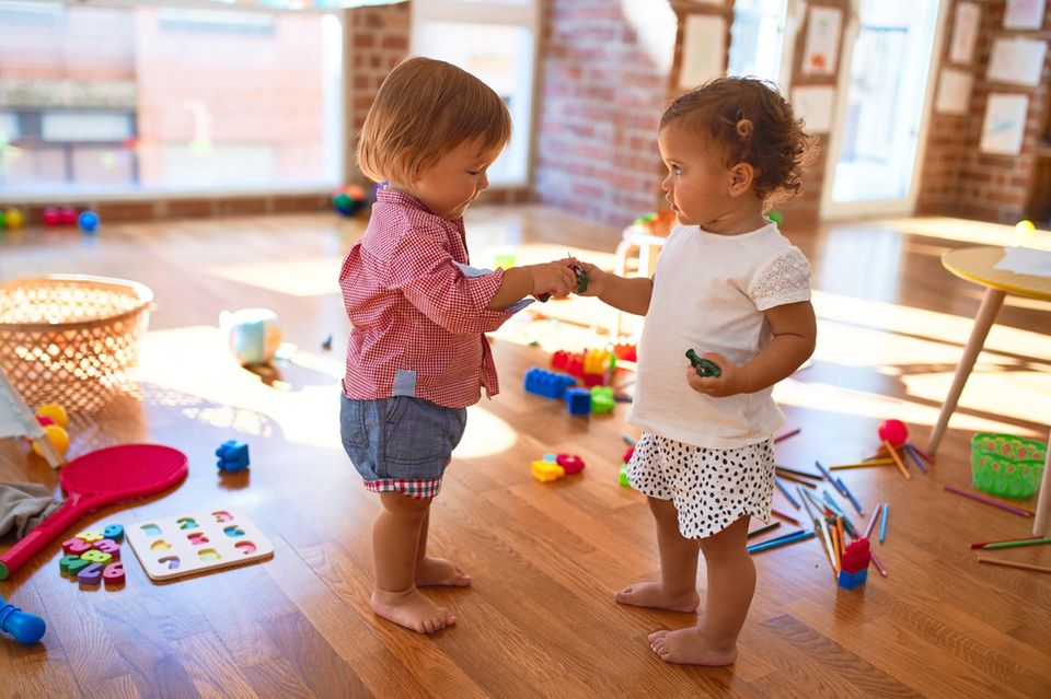 zwei Kleinkinder spielen miteinander in einem Raum mit Spielzeug
