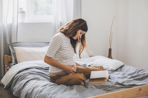 Schwangere sitzt im Bett und liest Buch