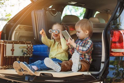 Packliste Familienurlaub: Zwei Kinder sitzen mit Gepäck im Kofferraum eines Autos