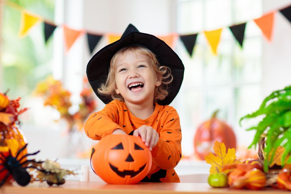 Kind mit Hexenhut freut sich über geschnitzten Halloween-Kürbis