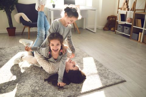 Zwei Mädchen toben mit der Mutter auf dem Teppich