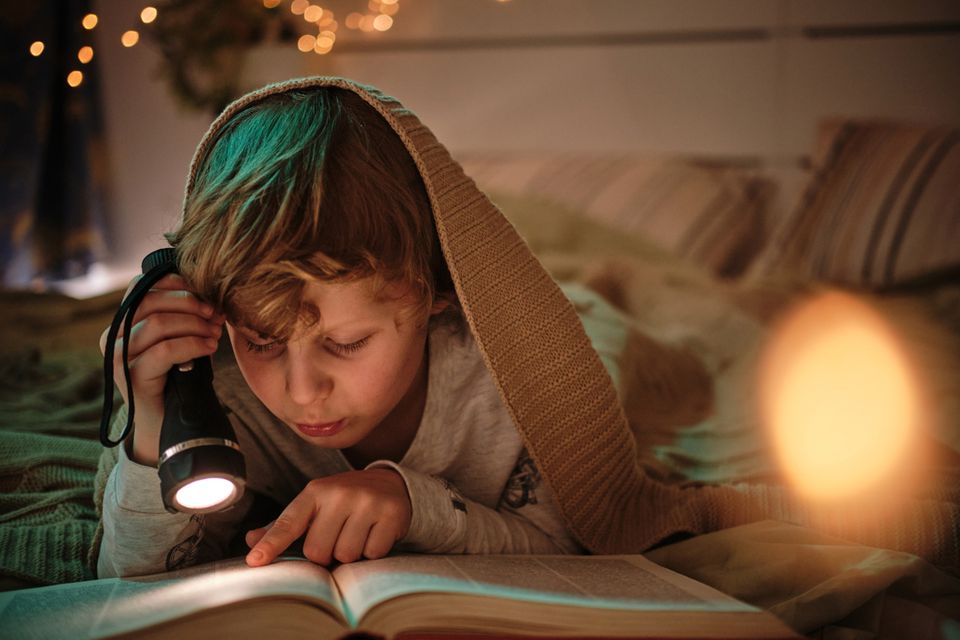 Taschenlampen für Kinder im Test: Junge liest mit Taschenlampe unter Bettdecke
