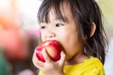 kleines asiatisches Mädchen beißt in einen roten Apfel