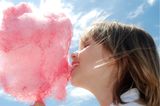 Mädchen beißt vor blauem Himmel in rosa Zuckerwatte
