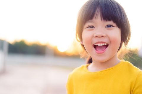 fröhlich lachendes asiatisches Mädchen im gelben Pullover