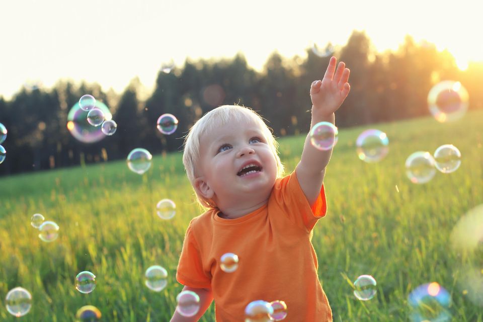 Weltentdecker: ein kleiner blonder Junge greift nach Seifenblasen auf einem Feld