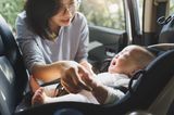 Entspannte Autofahrten mit Baby: Mutter beruhigt weinendes Baby im Autositz