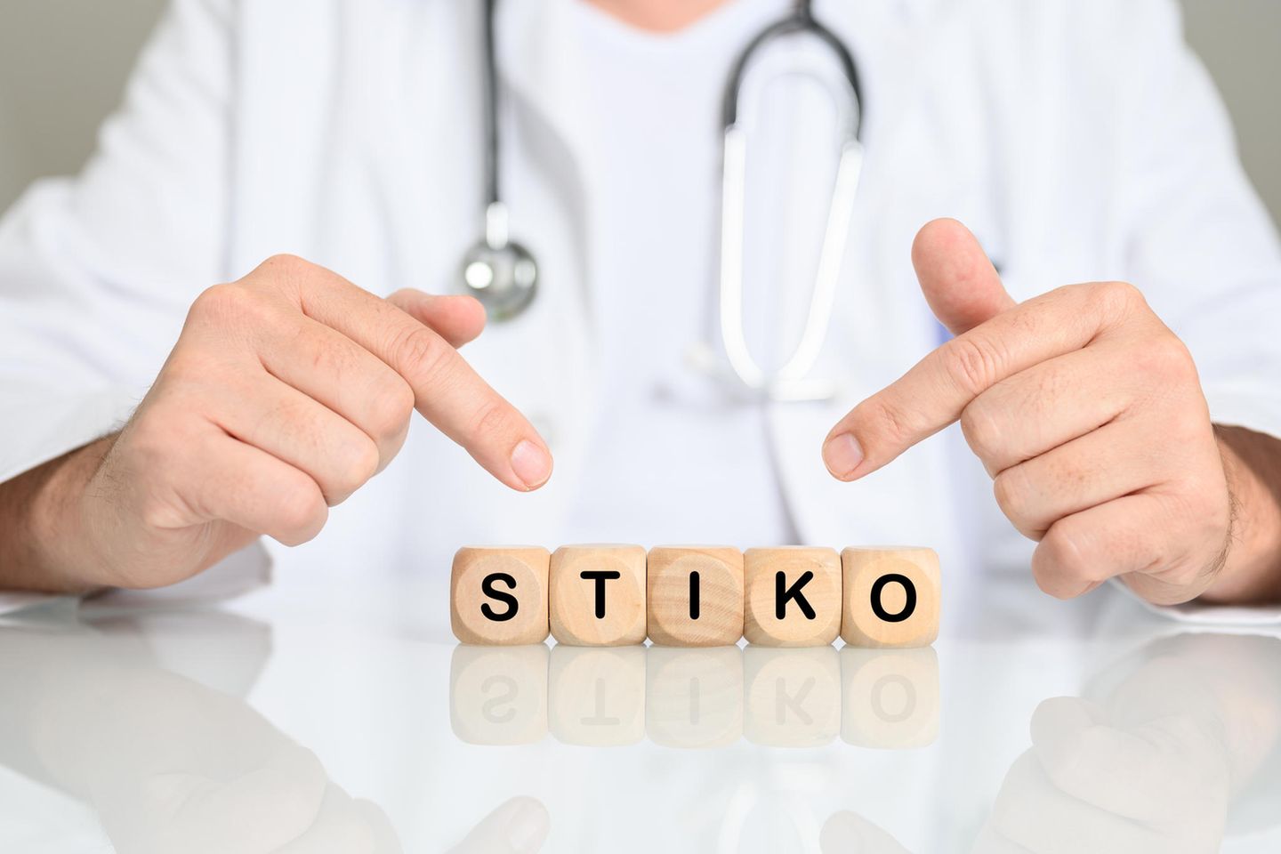 Mann mit Stethoskop zeigt auf Wort Stiko aus Buchstabenwürfeln
