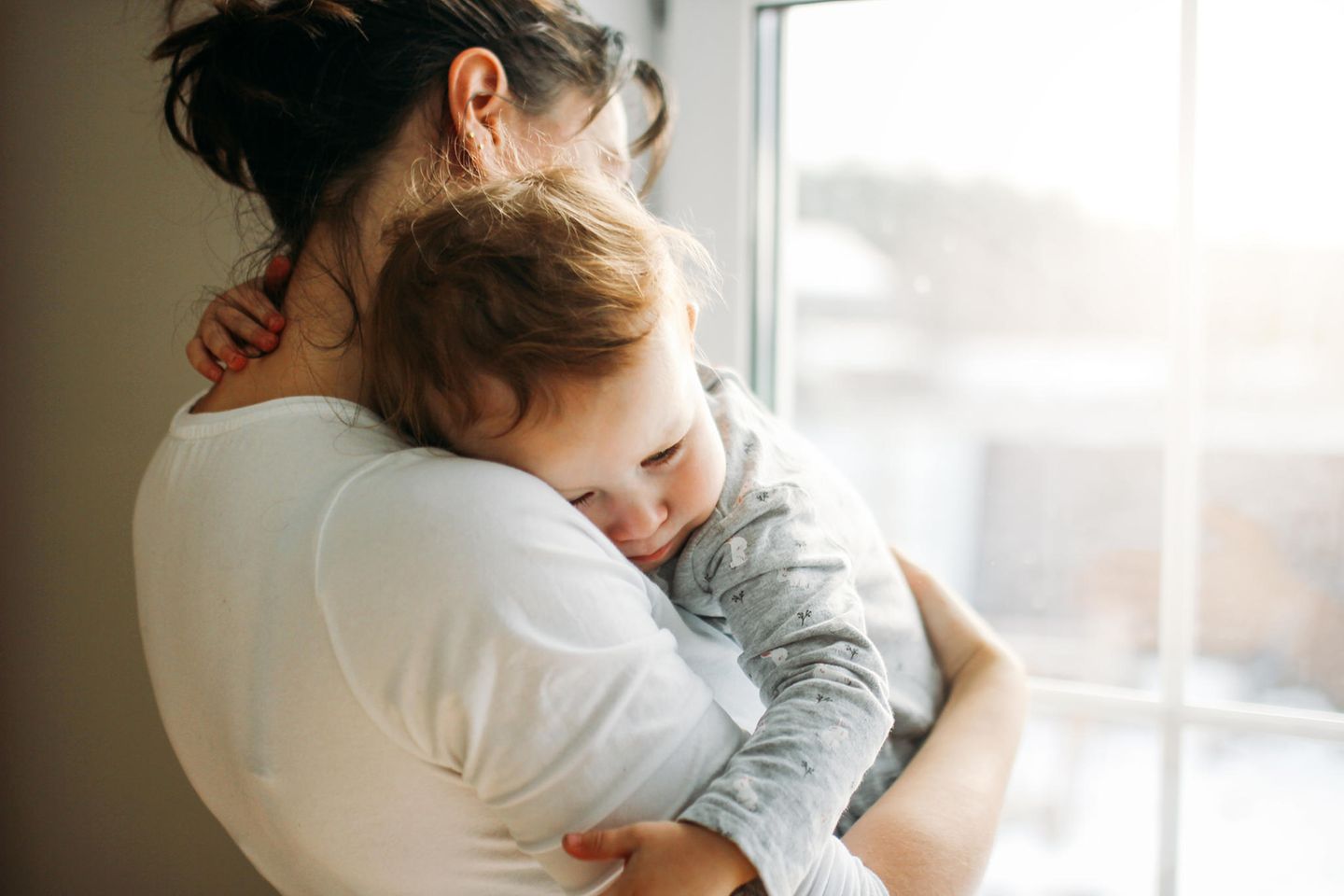 Schlafregression: Großes Baby oder Kleinkind liegt in den Armen seiner Mutter