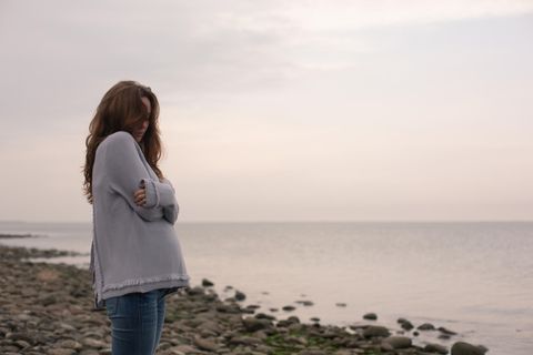 Schwangerschaftsdepressionen: Frau mit verschränkten Armen am Strand in Dämmerung